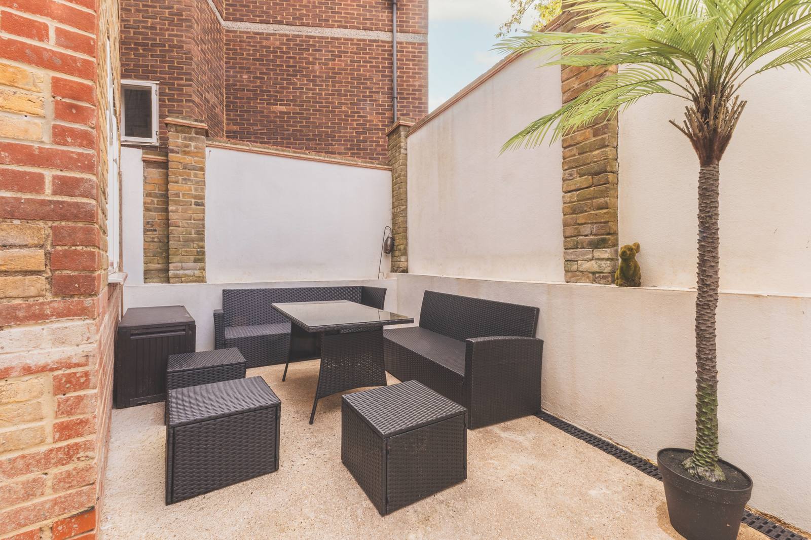 The walled courtyard with outdoor sofas, a table and a potted palm